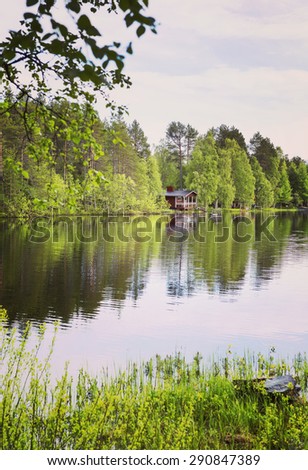 A beautiful scenery in Northern part of Finland in the summer time. On the other side of the lake is a small red sauna. Image has a vintage effect.