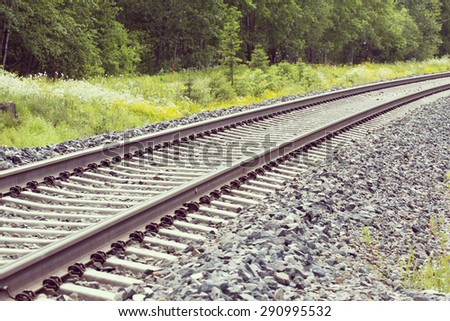 Railroad tracks in the summer time. Birch forest is surrounding the tracks. Image has a vintage effect.
