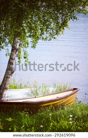 A traditional summer photo from Finland. A lonely boat next to a birch by the lake. Image has a vintage effect.
