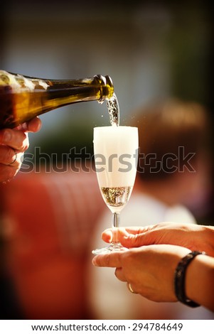 An image of pouring champagne to a glass outdoor in the summer time. Image also has a vintage effect.