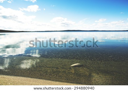 A beautiful scene with crystal clear water in Finland in the summer time. Some clouds in the sky giving a deep contrast to the image and a rock is visible through water. Image has a vintage effect.