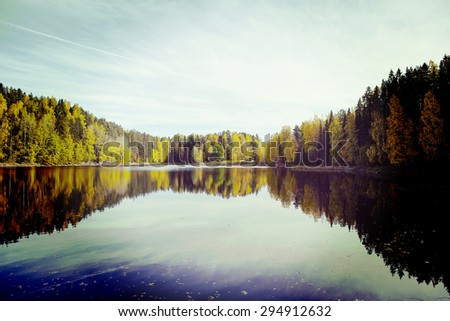 Amazing sunset scenery from Finland. Water and forest with reflections. Image has a vintage effect applied.