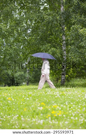 An elderly man is walking in the rain with an umbrella.