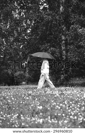A elderly man is walking in the rain with a black umbrella. Image has a vintage effect.