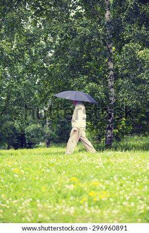 A elderly man is walking in the rain with a black umbrella. Image has a vintage effect.