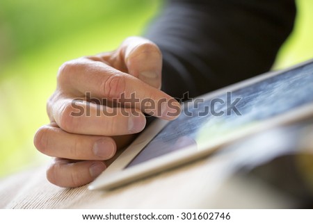 An older man is browsing the internet with a white tablet outdoor.