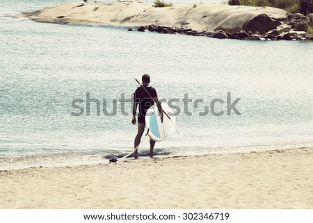A male surfer is carrying the surf board on the beach after a surfing session. Image has a vintage effect applied.