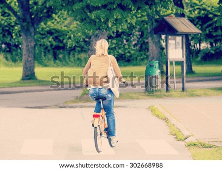 A blonde girl in a leather jacket is riding a bike in the streets on a summer day. Image has a strong vintage effect applied.