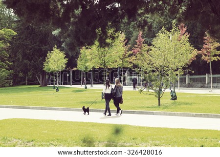 Couple of girls are walking the black dog in park during autumn time. Colorful trees are in the background. The dog breed is black german spitz. Image has a vintage effect applied.