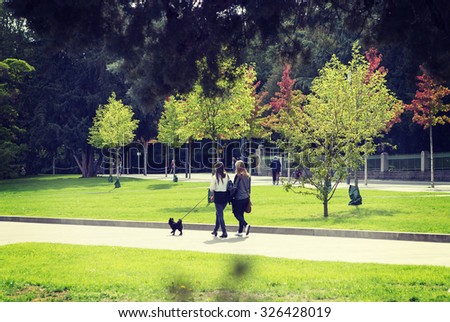Couple of girls are walking the black dog in park during autumn time. Colorful trees are in the background. The dog breed is black german spitz. Image has a vintage effect applied.