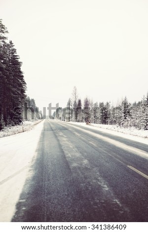A very slippery road during winter. Black ice is covering the whole road and it is dangerous to drive even with studded winter tires. Image has a vintage effect applied.