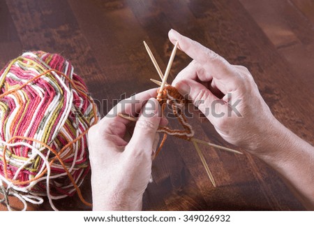 An elderly woman is knitting a sock on a kitchen table. It is a skill normally for elderly people.