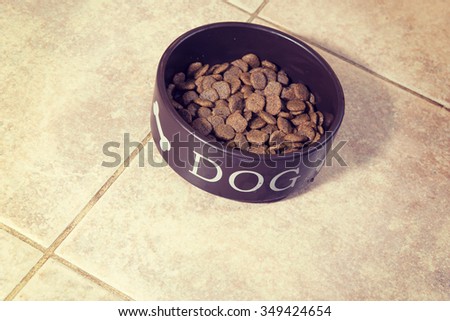 Dog food in a food bowl for dogs. The cup is on the kitchen floor. Image has a vintage effect applied.