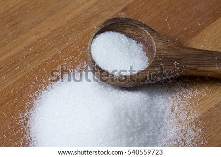 Wooden spoon with a pile of sugar or salt. Wooden surface.