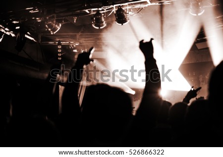 silhouettes of people at a concert in front of the scene in orange bright light. Hands with gesture Horns. That rocks