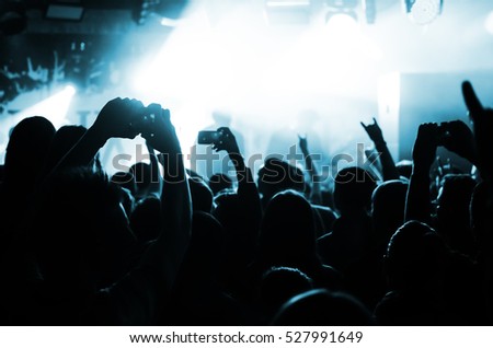 silhouettes of people at a concert in front of the scene in orange bright light. Hands with gesture Horns. That rocks