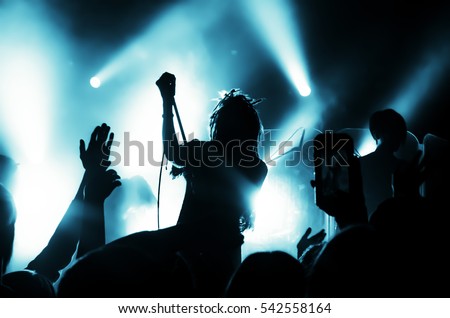Silhouette of musicians girl with dreadlocks on the stage during a rock concert in front of a crowd of fans. People in the bright light of the lanterns