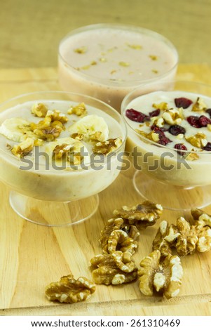 Three smoothies with different toppings of crushed walnuts, dried cherries and slice banana fruit.