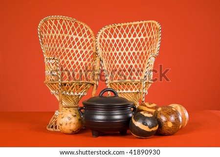 African woven bamboo chairs with seed pods and black cast iron pot on orange background