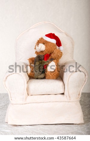 Marmoset monkey holding onto bear on mini chair, on ivory backdrop