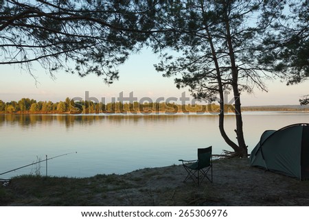 Scenic of tent, chair and rod ready for fishing on bank of calm river om early summer morning
