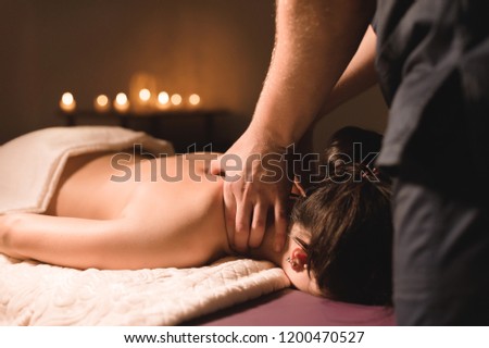 Men\'s hands make a therapeutic neck massage for a girl lying on a massage couch in a massage spa with dark lighting. Close-up. Dark Key