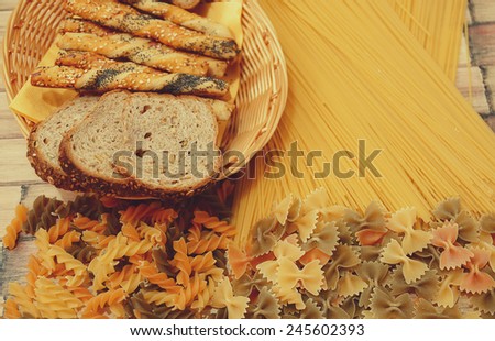 Variety of types and shapes of Italian pasta. Dry pasta background with slice of bread and salty sticks