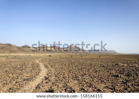 Morocco, Hamada du Draa (Draa stone desert) path with mountain in background