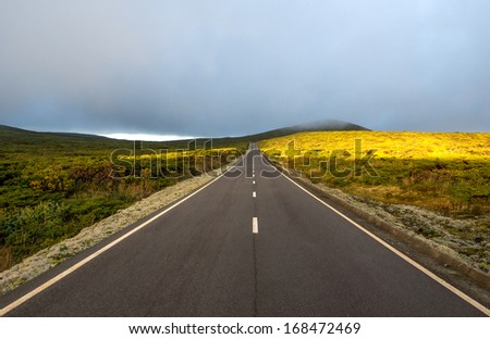 Road among hills with clouds and sun on Flores island, Azores archipelago (Portugal)
