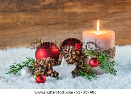 Christmas candle with traditional christmas decoration, red baubles, star, pine cones and green branches at snow