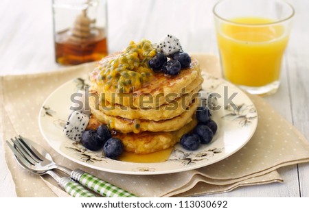A stack of low-fat tofu pancakes served with honey, blueberries and tropical fruits