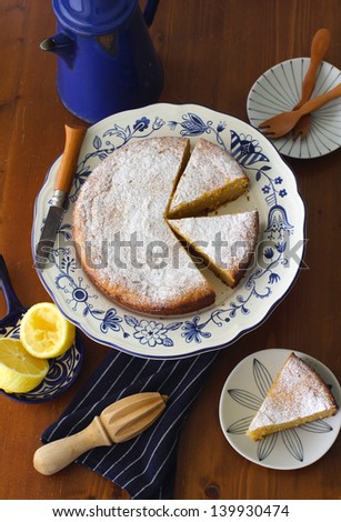 Aerial view of lemon ricotta cake, made with olive oil, ground almond and honey, served on a pattern cake platter, on a rustic wood surface