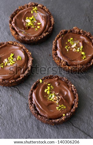 4 individual chocolate avocado pudding whole grain tarts on a black slate stone surface, sprinkled with pistachio and sea salt