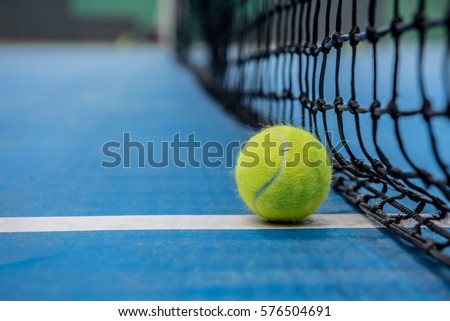 Yellow tennis ball on blue hard court and black net
