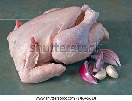 Whole fresh chicken on glass chopping board with spanish onion and garlic cloves
