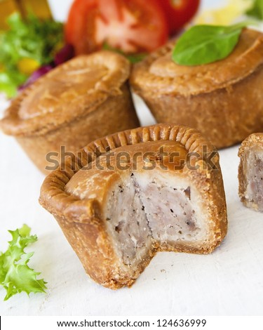 Crusty English pork pie sliced against a background of pies green leaf salad and tomatoes