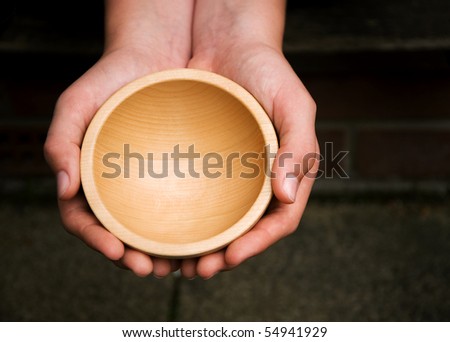 White hands holding a wooden begging bowl