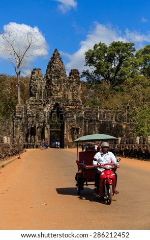 Siem Reap, Cambodia - Jan 8, 2015 : Angkor Thom face tower with line of gods statues on the left and demon statues on the right. A man driving local famous auto rickshaws called tuk-tuk.