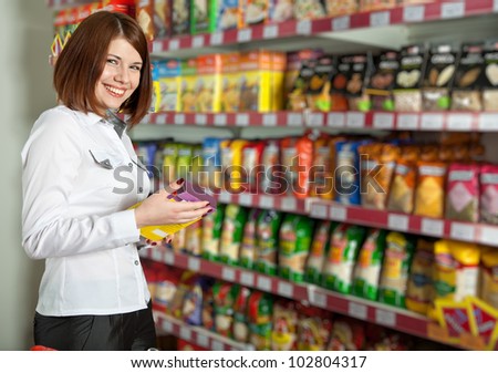 Pretty woman buyer in grocery shop at shelves with products