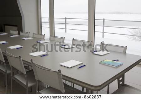Notebooks laying on a grey table with grey chairs in a meeting room