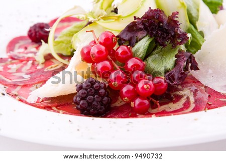 Plate with red berries, meat, a blackberry and leaves of salad and cheese
