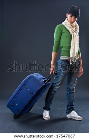 The young girl in a scarf and jeans with a dark blue suitcase on a dark background