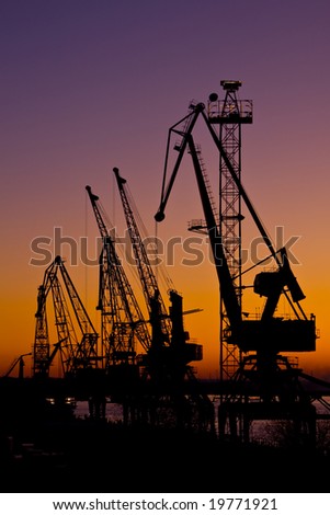 Silhouette of several cranes in a harbor,  sunset.