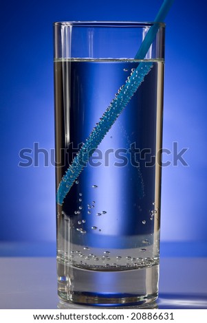 Glass with pure water with blue straw on a blue background