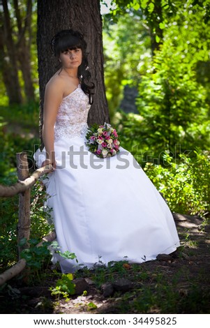 The bride with a bunch of flowers on a tree in wood Bride portrait in wedding dress sitting in wood