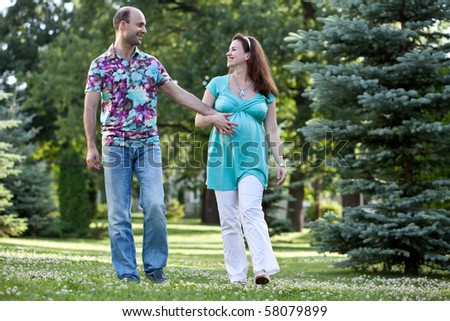 Happy couple, the pregnant wife and the husband, having joined hands walk in park