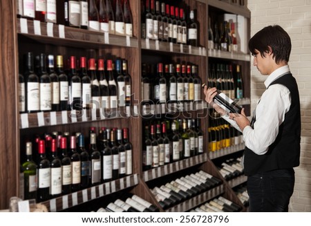 man looking at bottle of wine in supermarket.