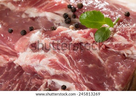 Fresh raw pork on light wooden cutting board with onion, garlic, pepper and vegetable oil