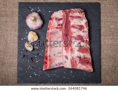 Fresh pork ribs, meat marinated and prepared for roast with garlic allspice on black background top view