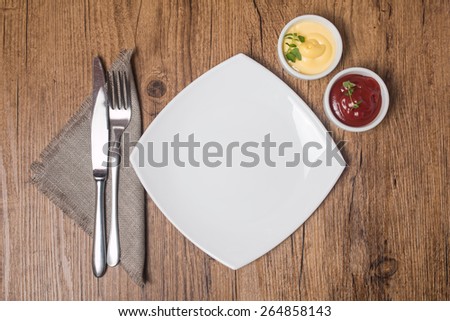 empty plate with fork and knife, ketchup and mayonnaise on the wooden table